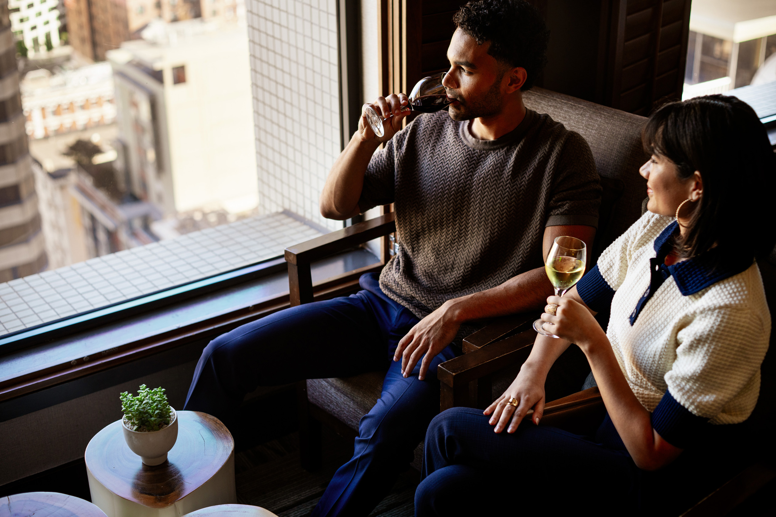 Guest sipping wine beside city window
