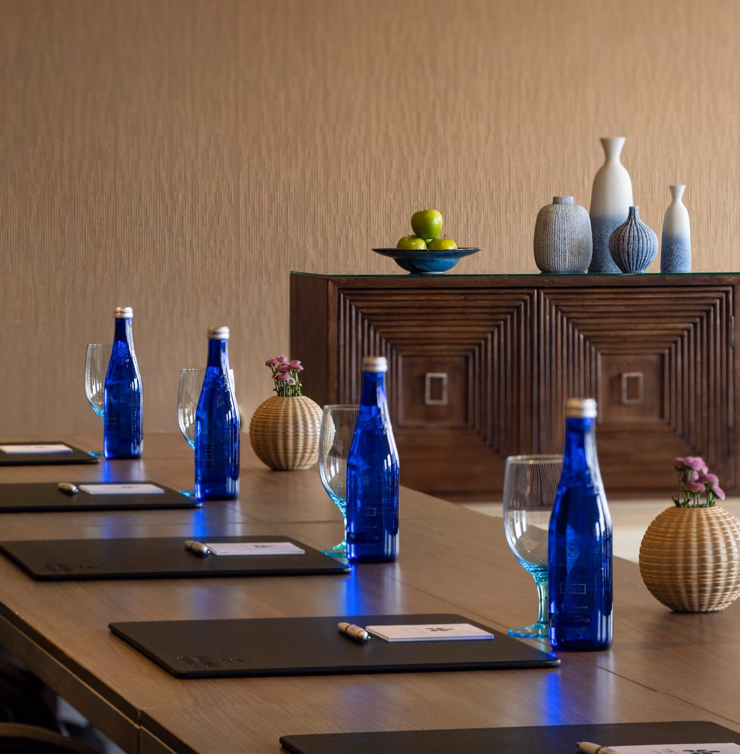 Conference table with blue Saratoga water bottles, glasses, notepads, pens, and vases with flowers.