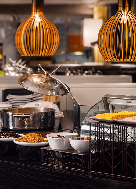 Buffet setup with large metal pot, bowls of snacks, and yellow sliced food plates under hanging lamps.