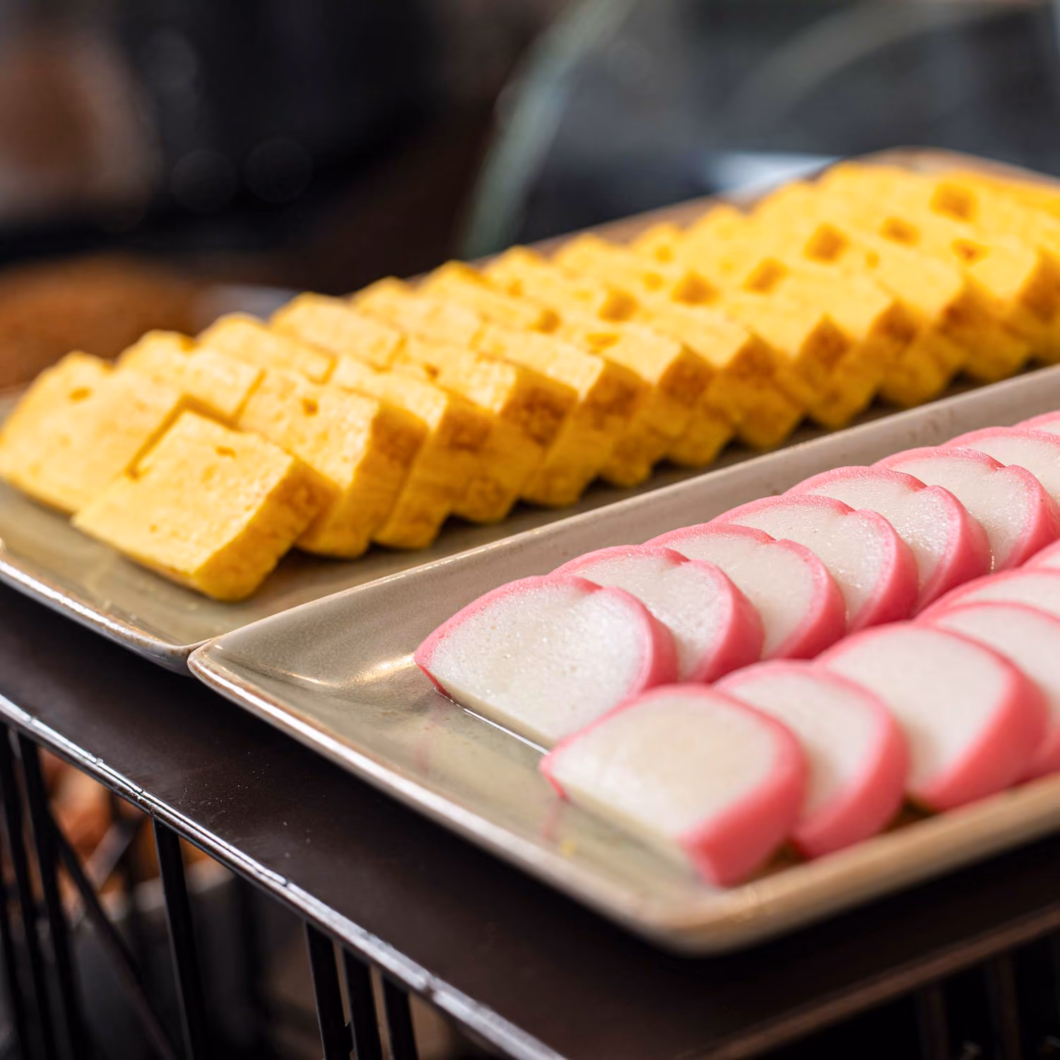 Plates of neatly sliced yellow tamagoyaki and pink-edged kamaboko on a buffet table.