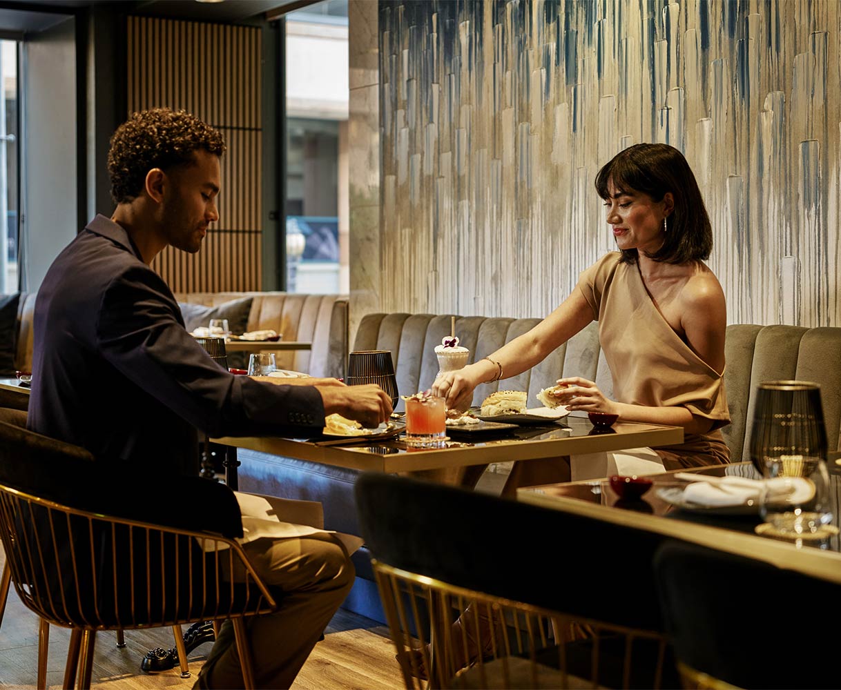 Couple dining at a restaurant table with drinks and food in a modern, stylish setting.