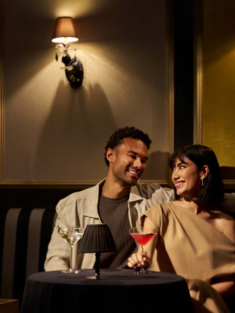 Smiling couple enjoying drinks in a dimly lit cozy lounge with a small table lamp.