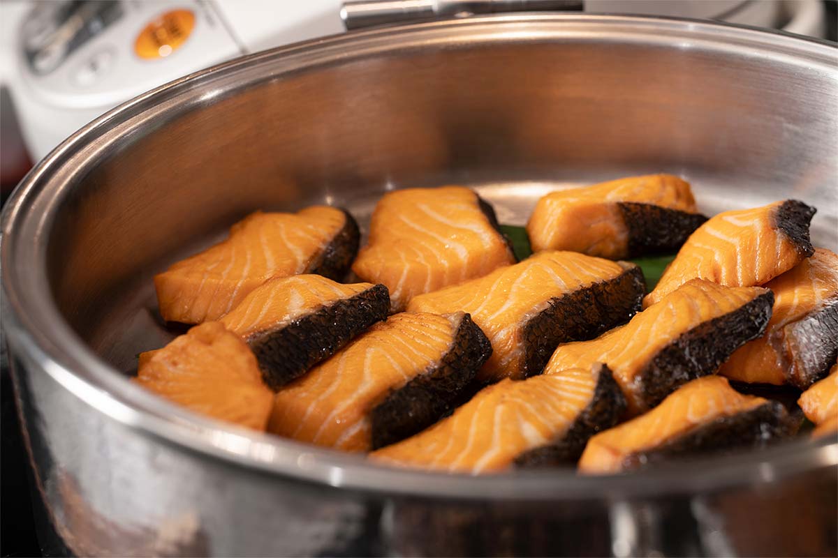 Pieces of cooked salmon with skin in a round metal serving dish.