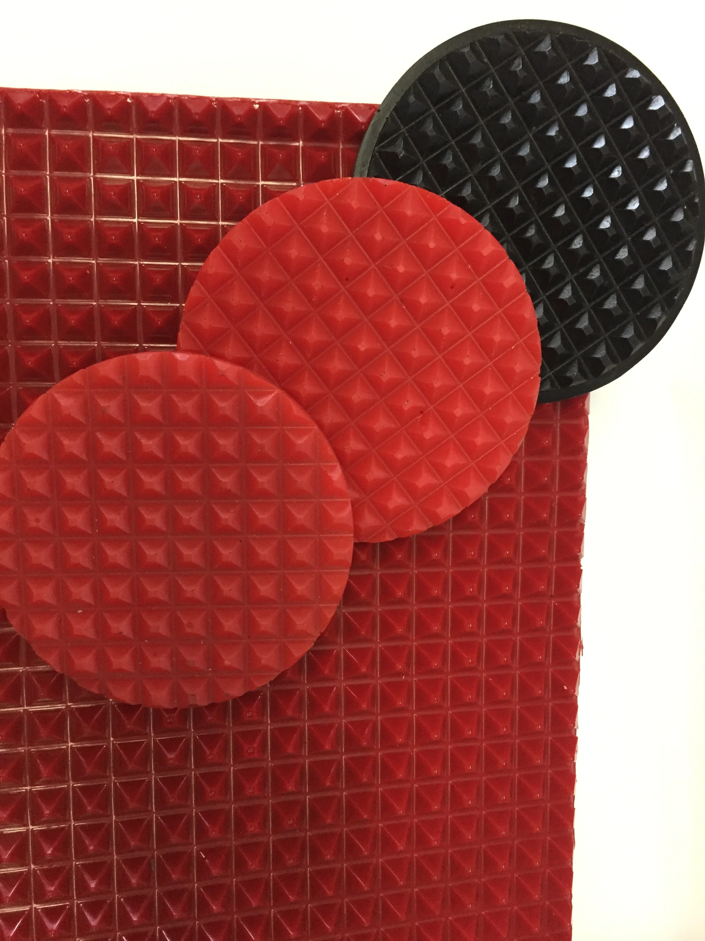Coussinets ronds de pont élévateur en polyuréthane rouge et noir à surface pyramidale, posés sur une plaque texturée moulée