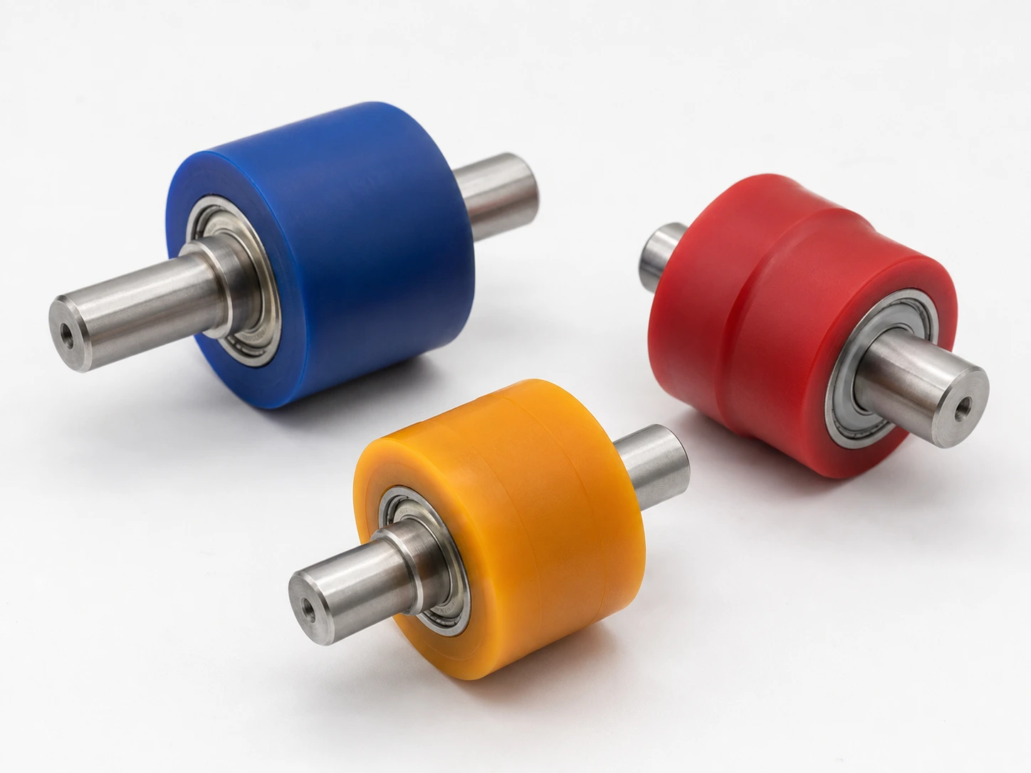 Trois galets de guidage en polyuréthane bleu, rouge et orange sur axes avec roulements — dureté choisie selon la charge