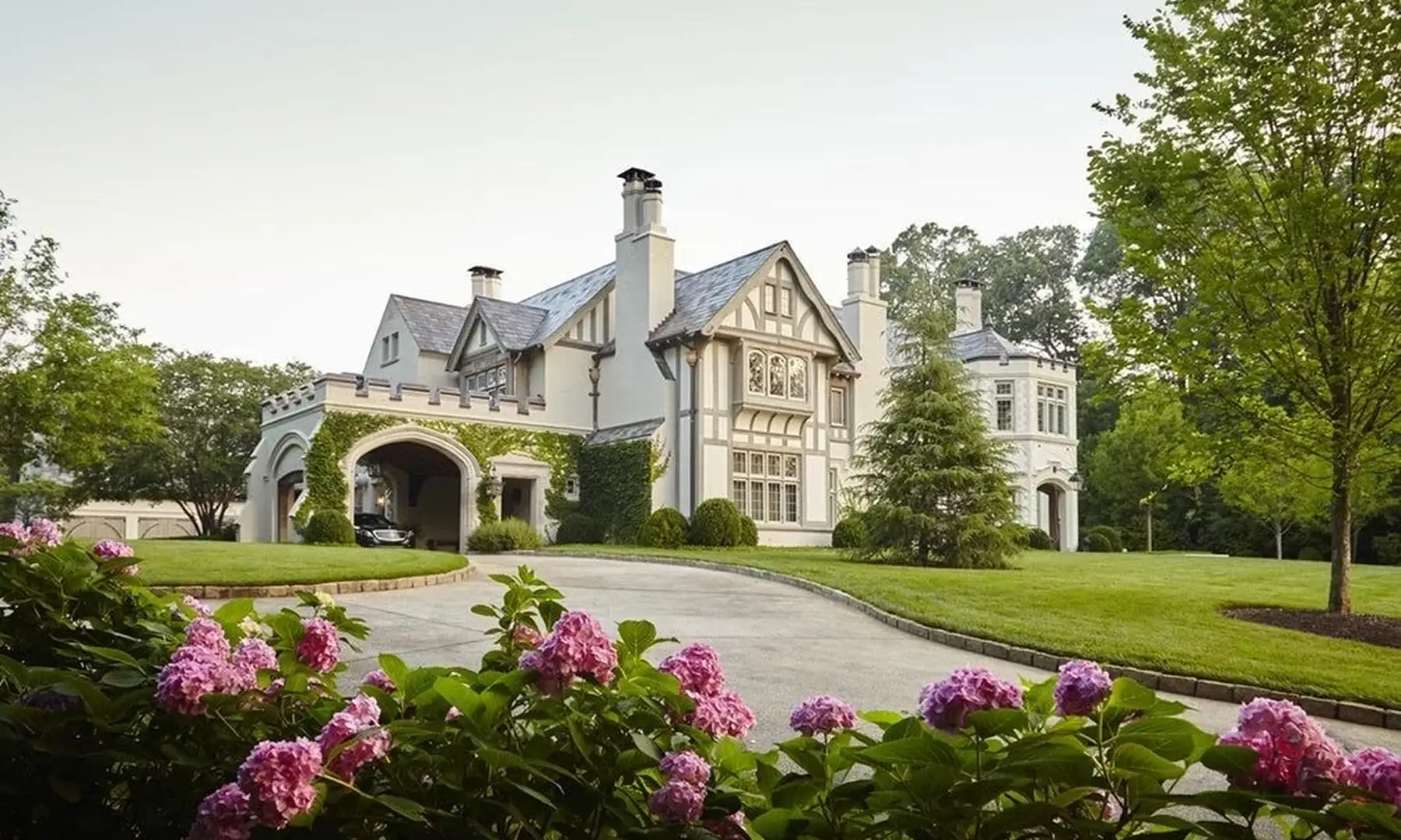 A Tudor-style estate behind a lawn and blooming pink hydrangeas