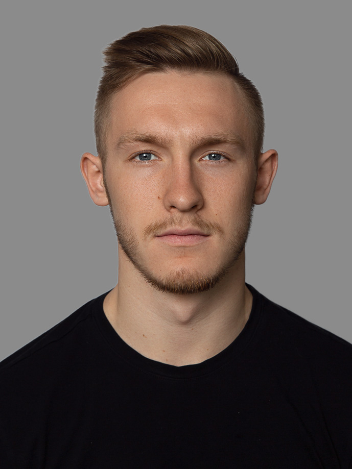 Young man with light brown hair and beard wearing a black shirt against a gray backdrop.