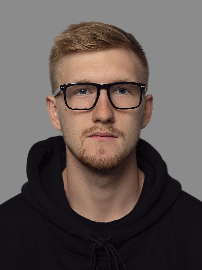 Young man with short blond hair, glasses, and a black hoodie looking straight at the camera.