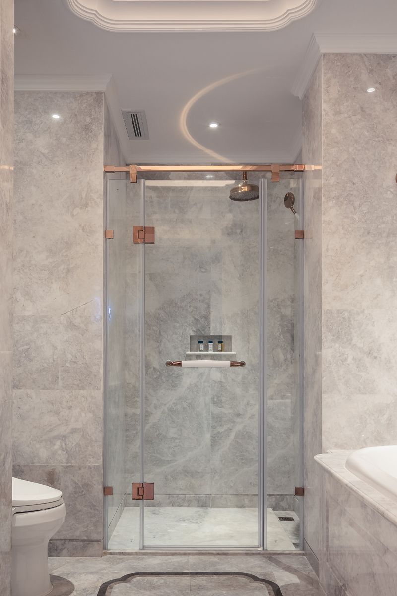 Luxury marble walk-in shower remodel with rose-gold fixtures by Coastal Builders Associates