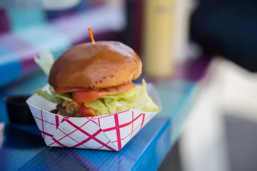 Burger with lettuce and tomato in a paper food tray on a blue table.