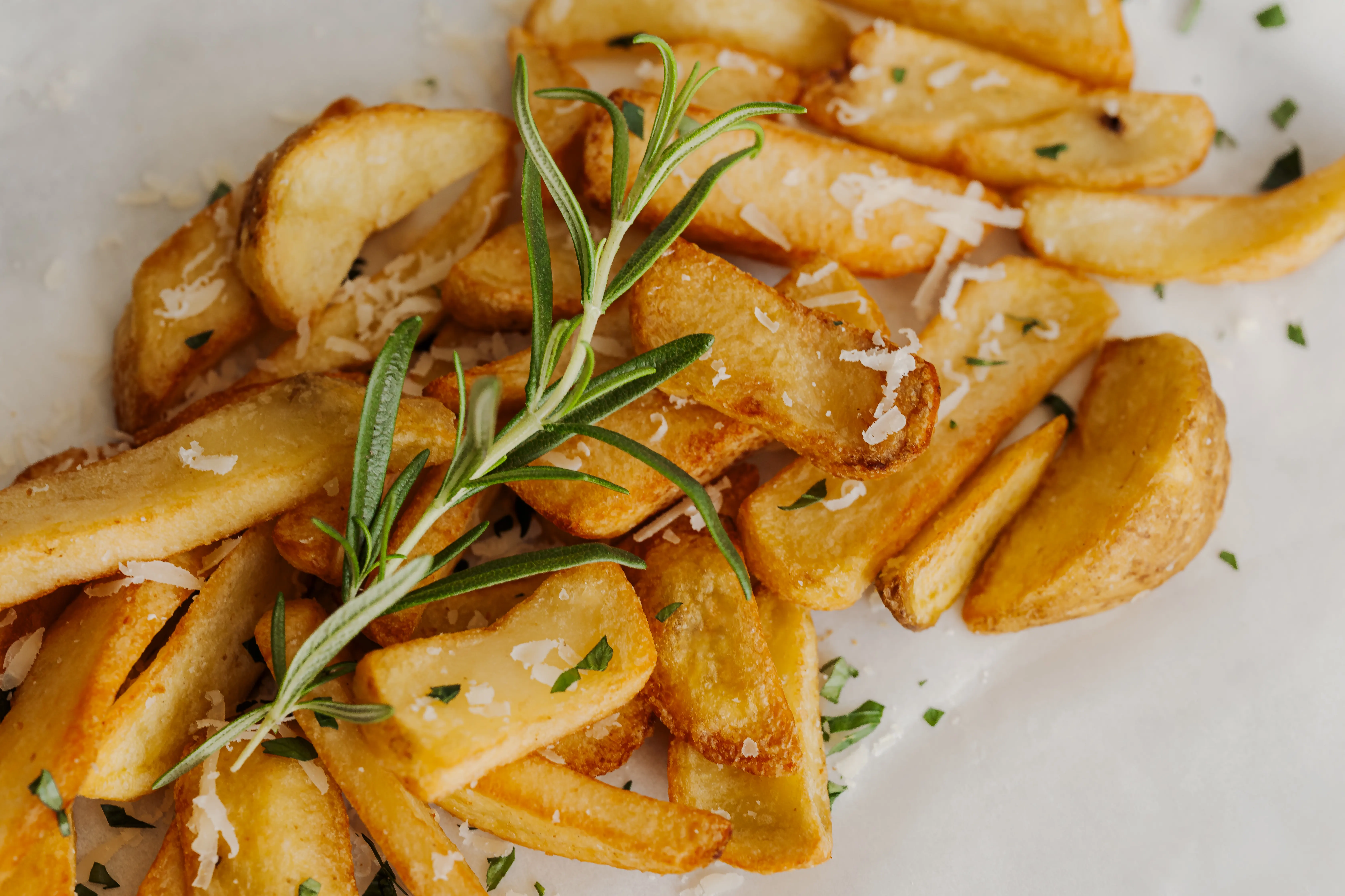 Golden fried potato wedges garnished with green herbs and grated cheese on a white surface.