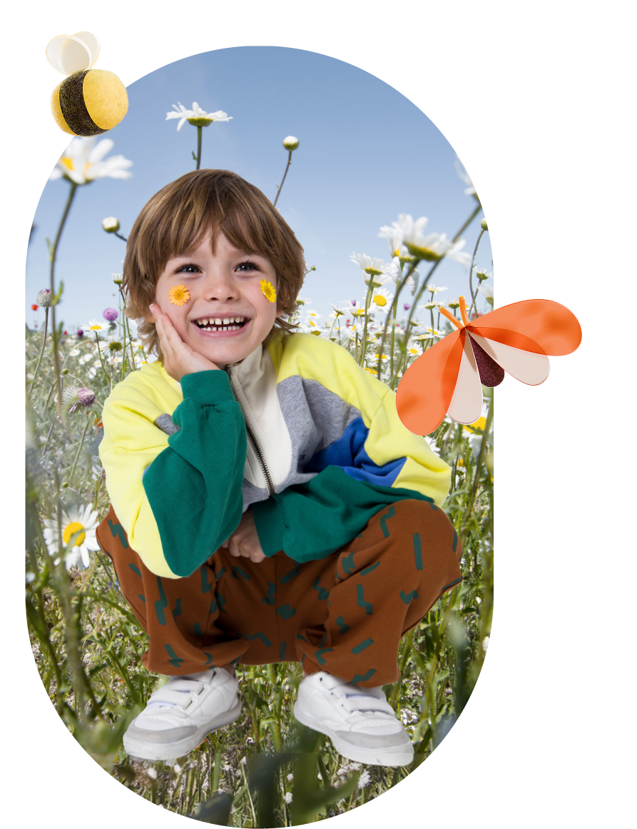 Smiling child with flower stickers on cheeks squatting in a daisy field under blue sky with bee and butterfly icons.