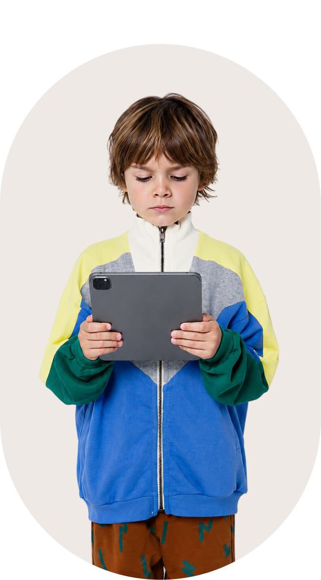 Boy wearing colorful jacket using a tablet with focused expression on a light background.