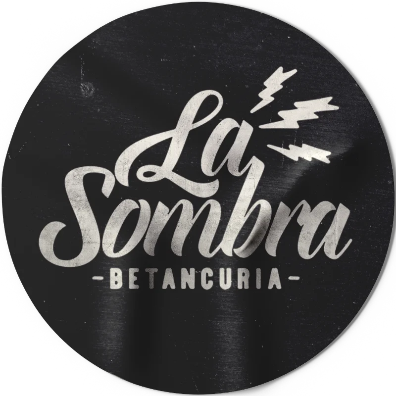 Circular black logo with white stylized text 'La Sombra' and smaller text 'Betancuria' below, with three lightning bolts above the text.