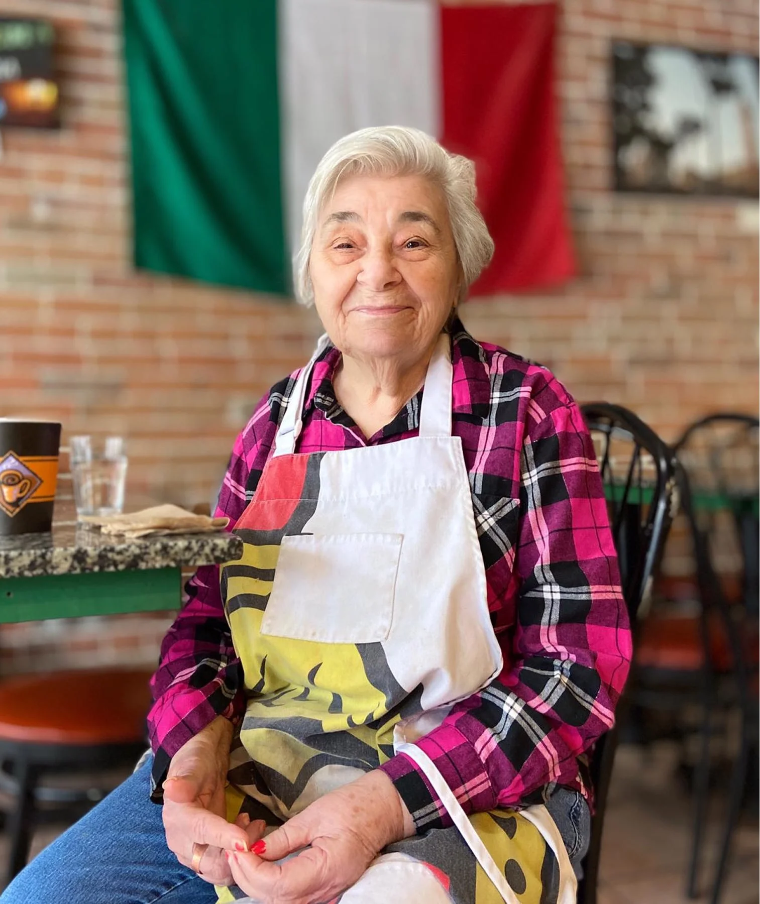 Portrait of Olga, founder of Olga's Deli, wearing a plaid shirt and apron.