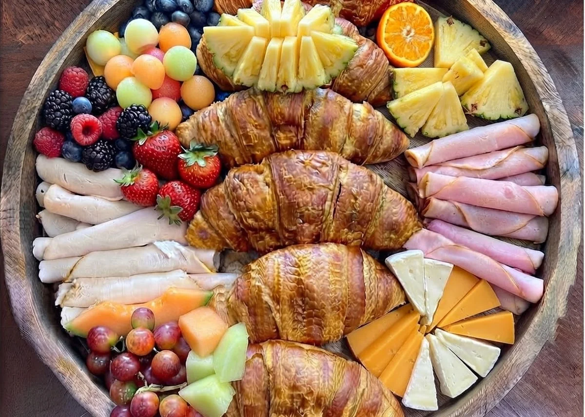 Morning Sunshine catering board with croissants, sliced deli meats, cheeses, and fruit.