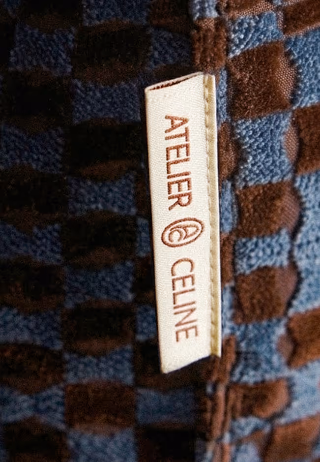 Clothing label reading 'Atelier Celine' on textured fabric with blue and brown squares.