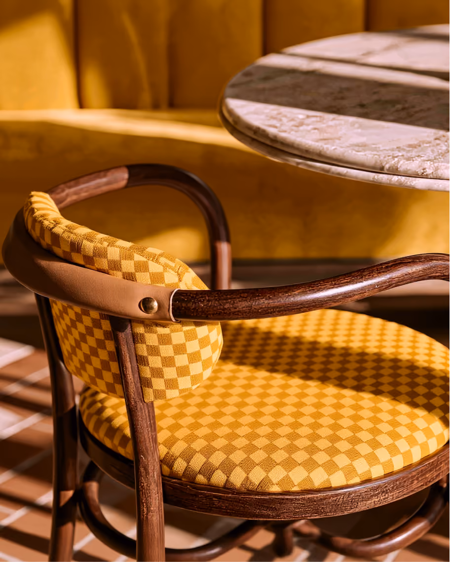 Wooden chair with yellow checkered cushion and marble table in warm sunlight.