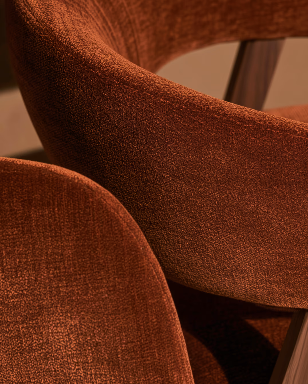 Close-up of two chairs with curved backs upholstered in a rust-colored textured fabric.