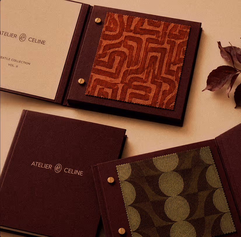 Brown fabric swatch books from Atelier Celine with geometric textile patterns, laid on beige surface.