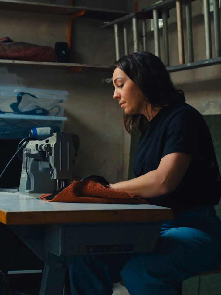 Woman working on an industrial sewing machine with orange fabric in a workshop.