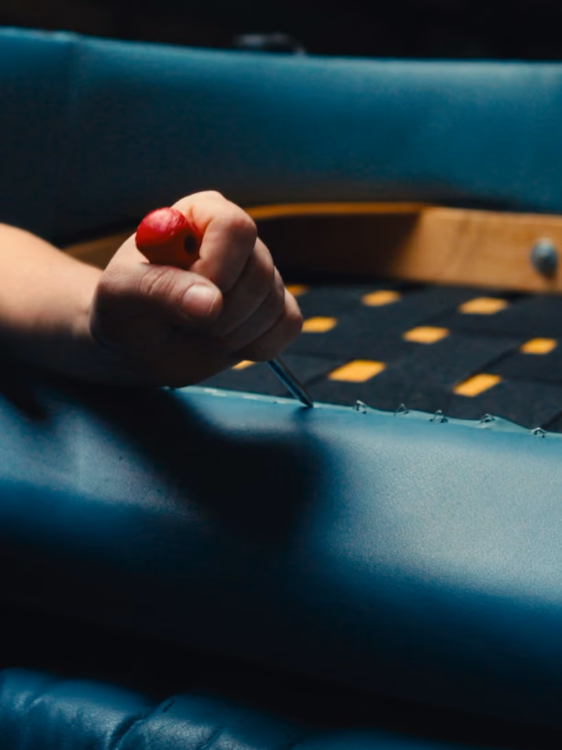 Hand using a red-handled tool to repair or remove upholstery on a blue chair frame.