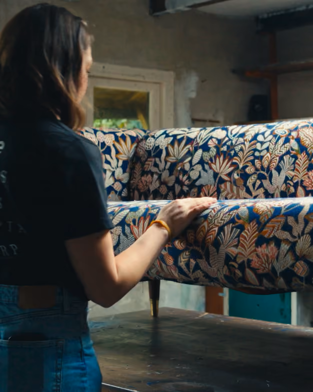 Person touching a floral-patterned upholstered couch in a workshop setting.