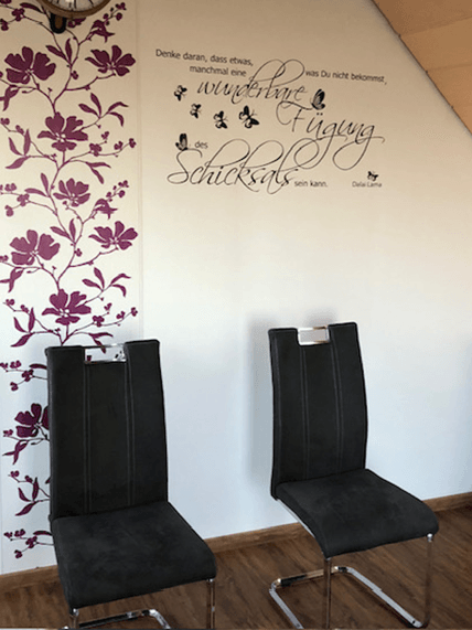 Zwei schwarze Stühle vor einer Wand mit lila Blumenmuster und einem Zitat von Dalai Lama.
