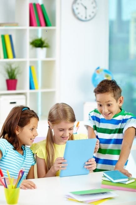 Drei Schulkinder schauen gemeinsam lächelnd auf ein Tablet