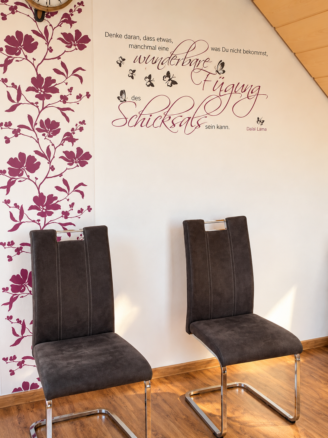 Zwei schwarze Stühle vor einer Wand mit lila Blumenmuster und einem Zitat von Dalai Lama.