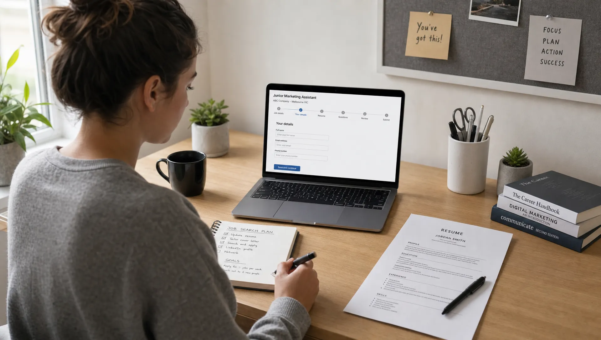 A job seeker sits at a tidy desk with a notebook, printed resume draft and laptop open to a job application page, planning next steps for an entry-level job search.