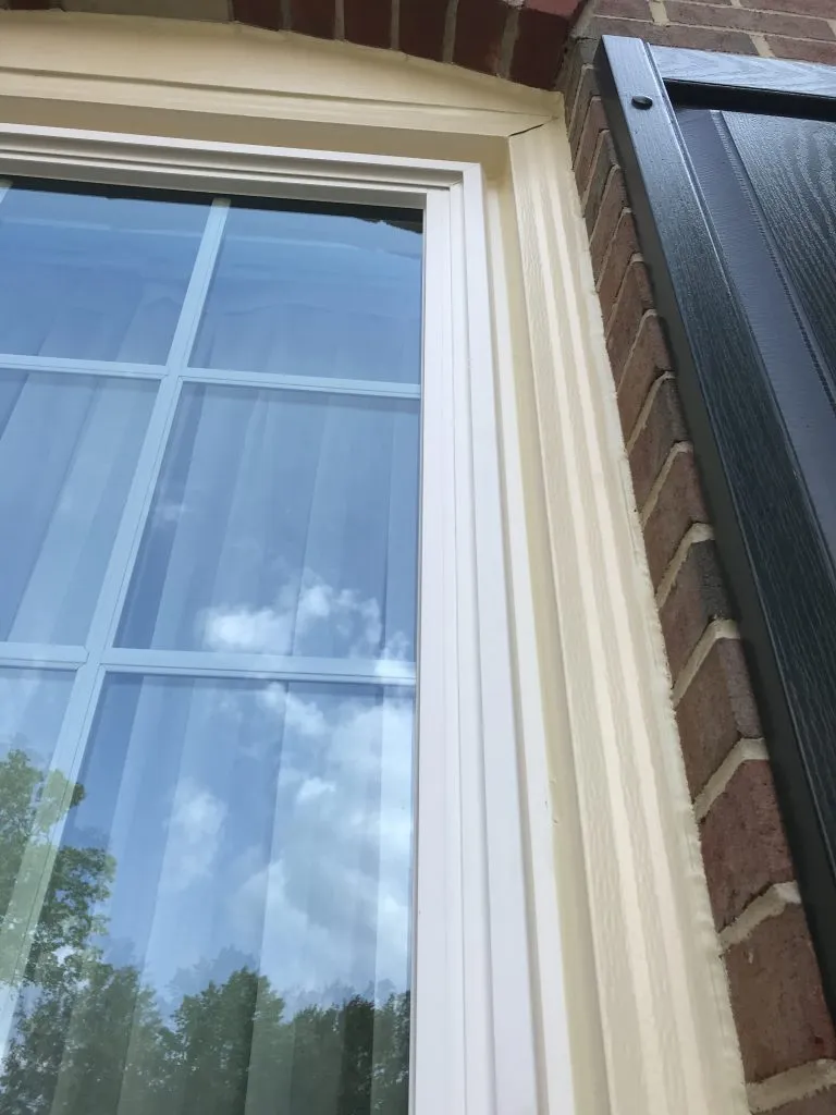 Close-up of a new double-hung window with cream trim beside a black shutter on a brick home