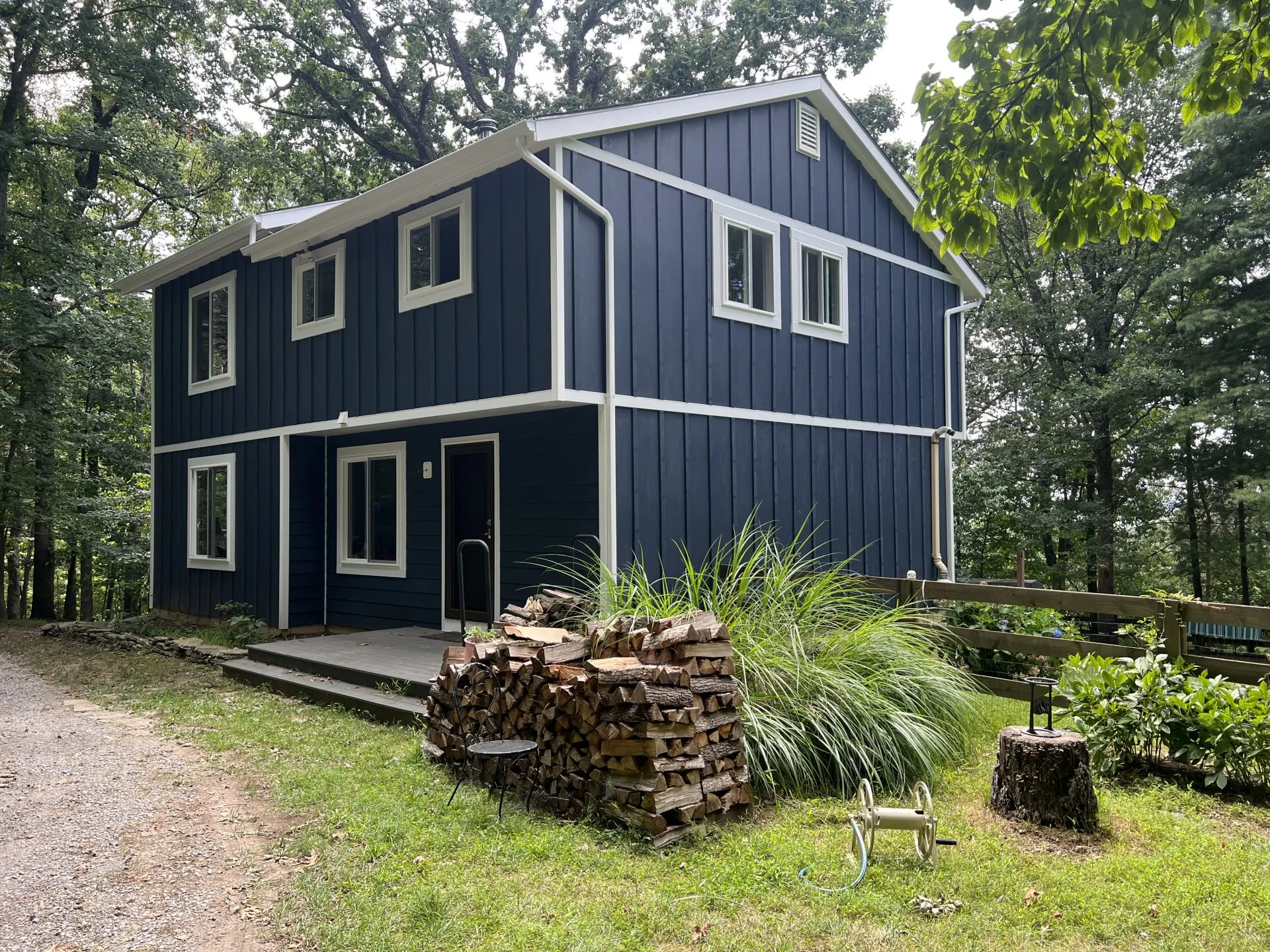 Navy blue board-and-batten siding with white trim on a wooded two-story home