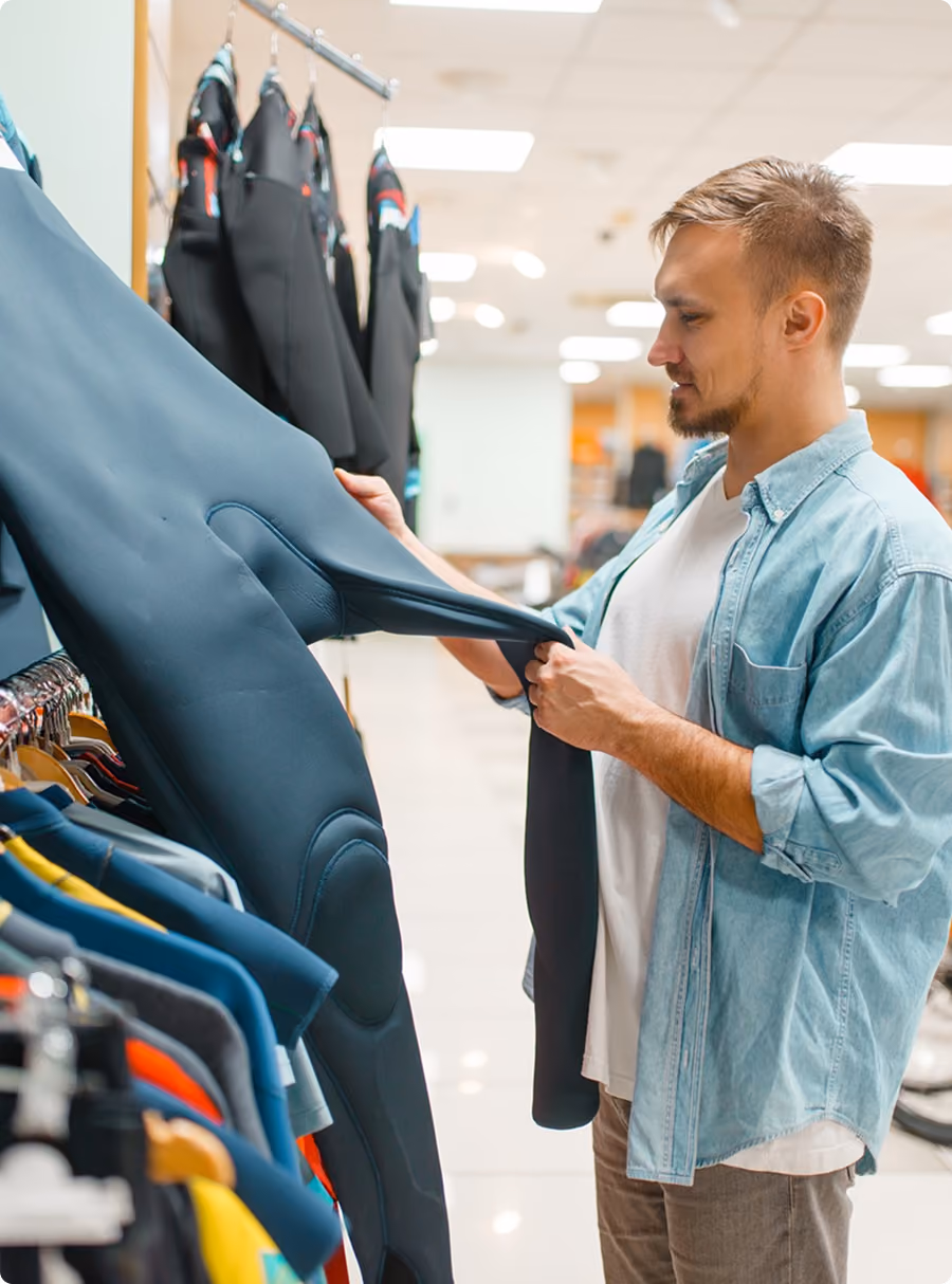 Man examining a black wetsuit on a clothing rack in a store.