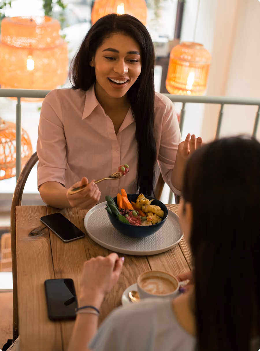 Two women dining together, one eating a bowl of food and the other holding a cup of coffee.