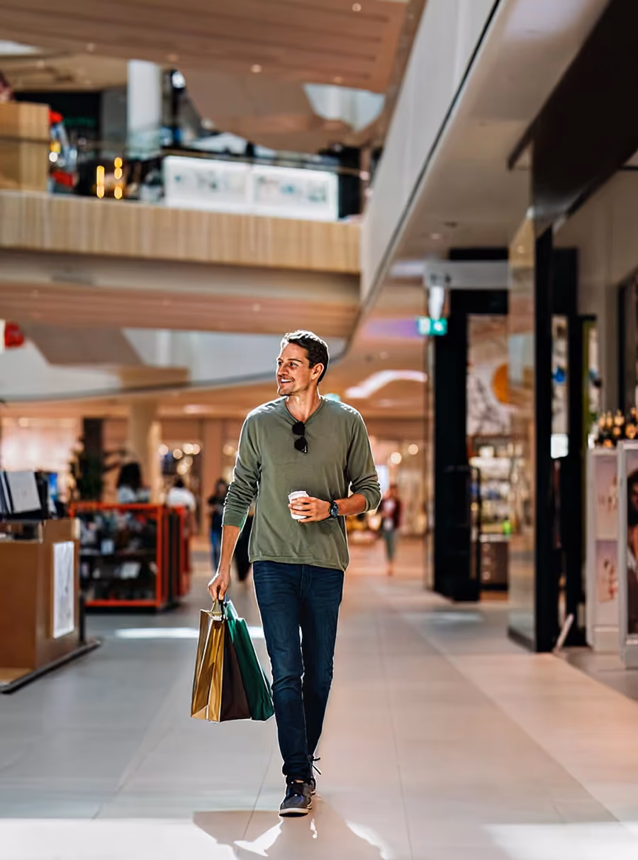 Smiling man holding shopping bags and a coffee cup walking in a shopping mall.