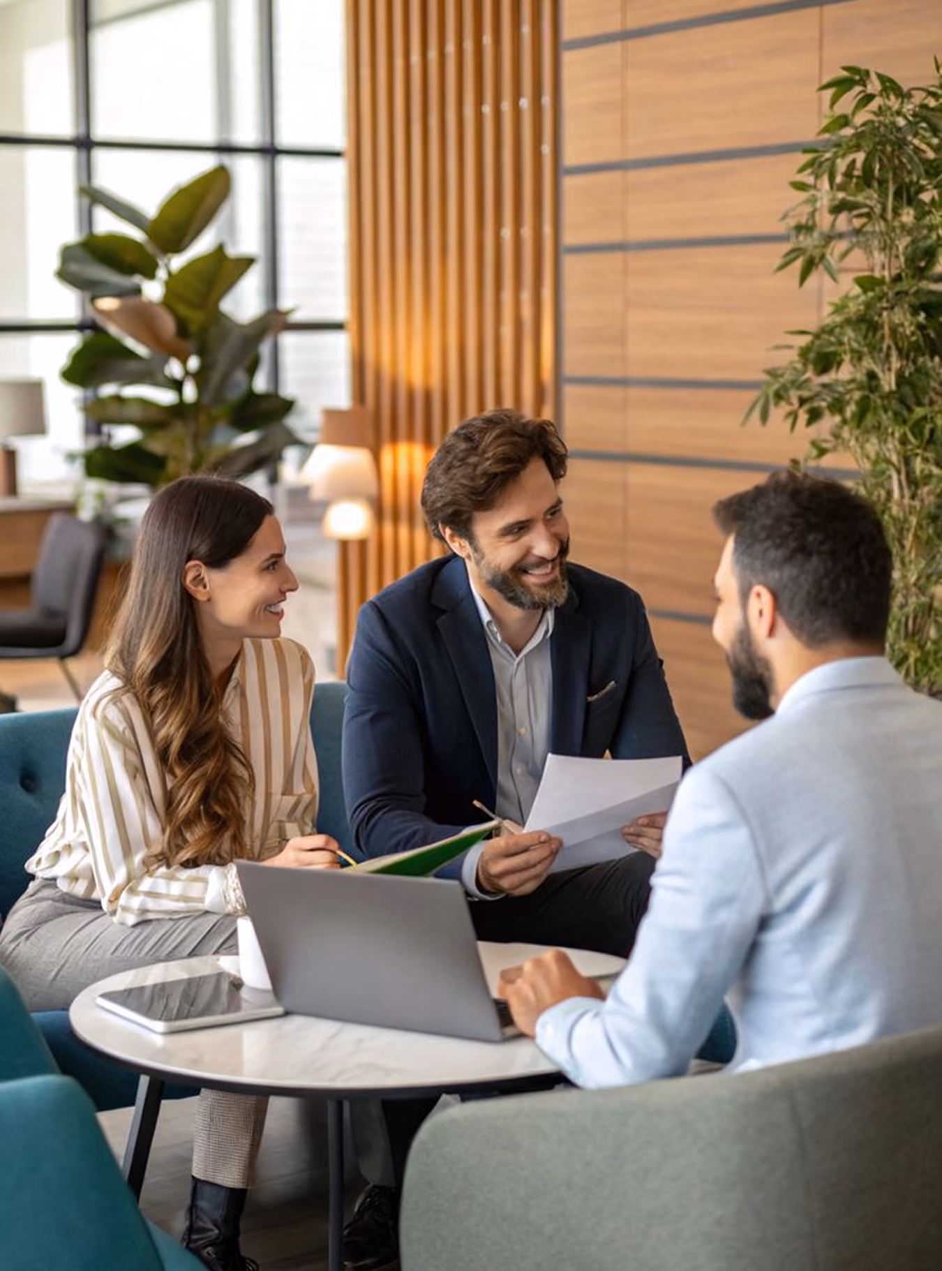 Three professionals having a meeting around a coffee table with a laptop and documents in a modern office.
