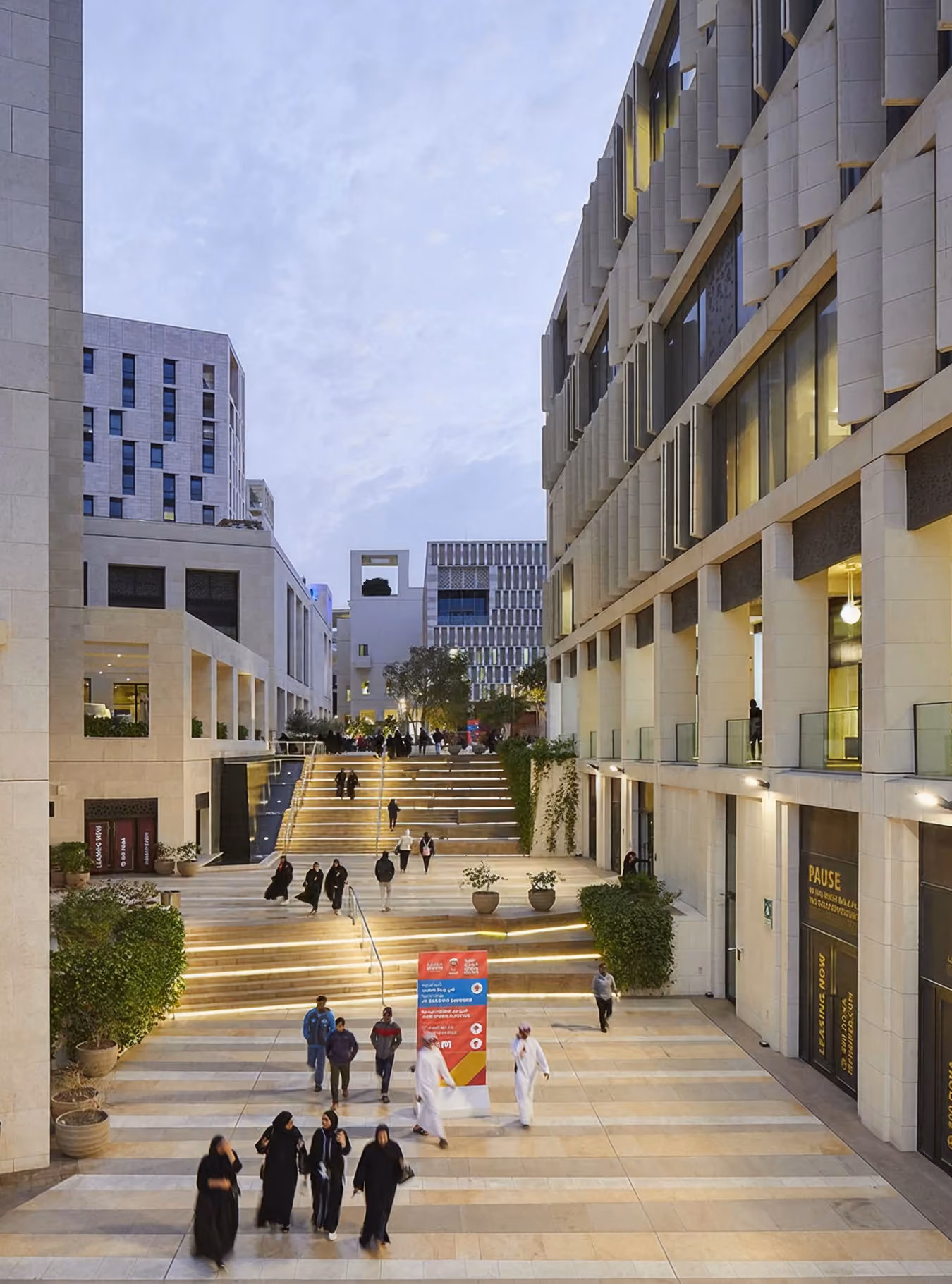 People walking in a modern outdoor plaza with steps lit by yellow lights and tall buildings.