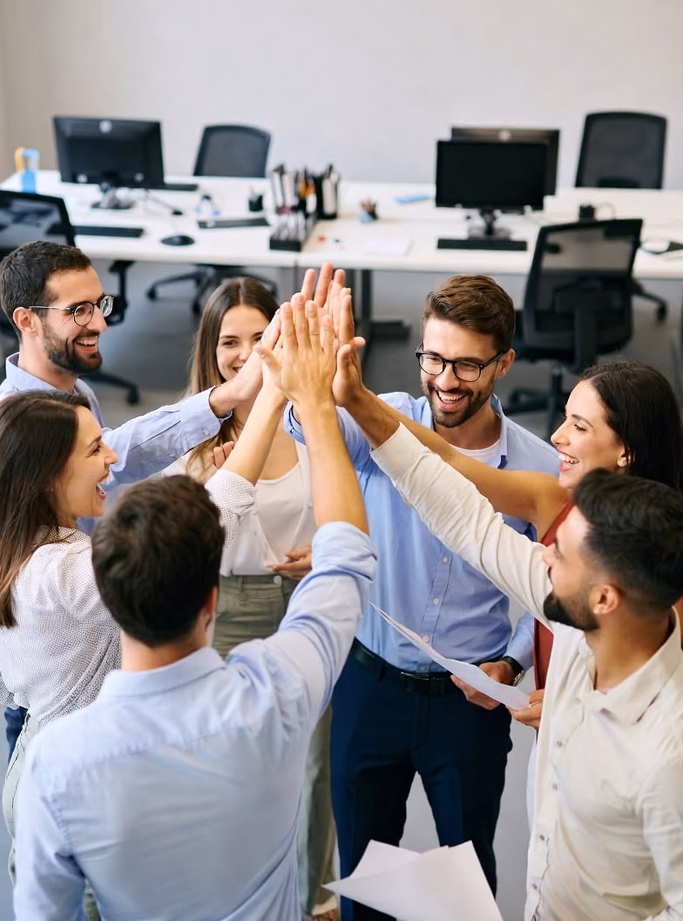 Group of six coworkers smiling and giving a group high-five in an office setting.