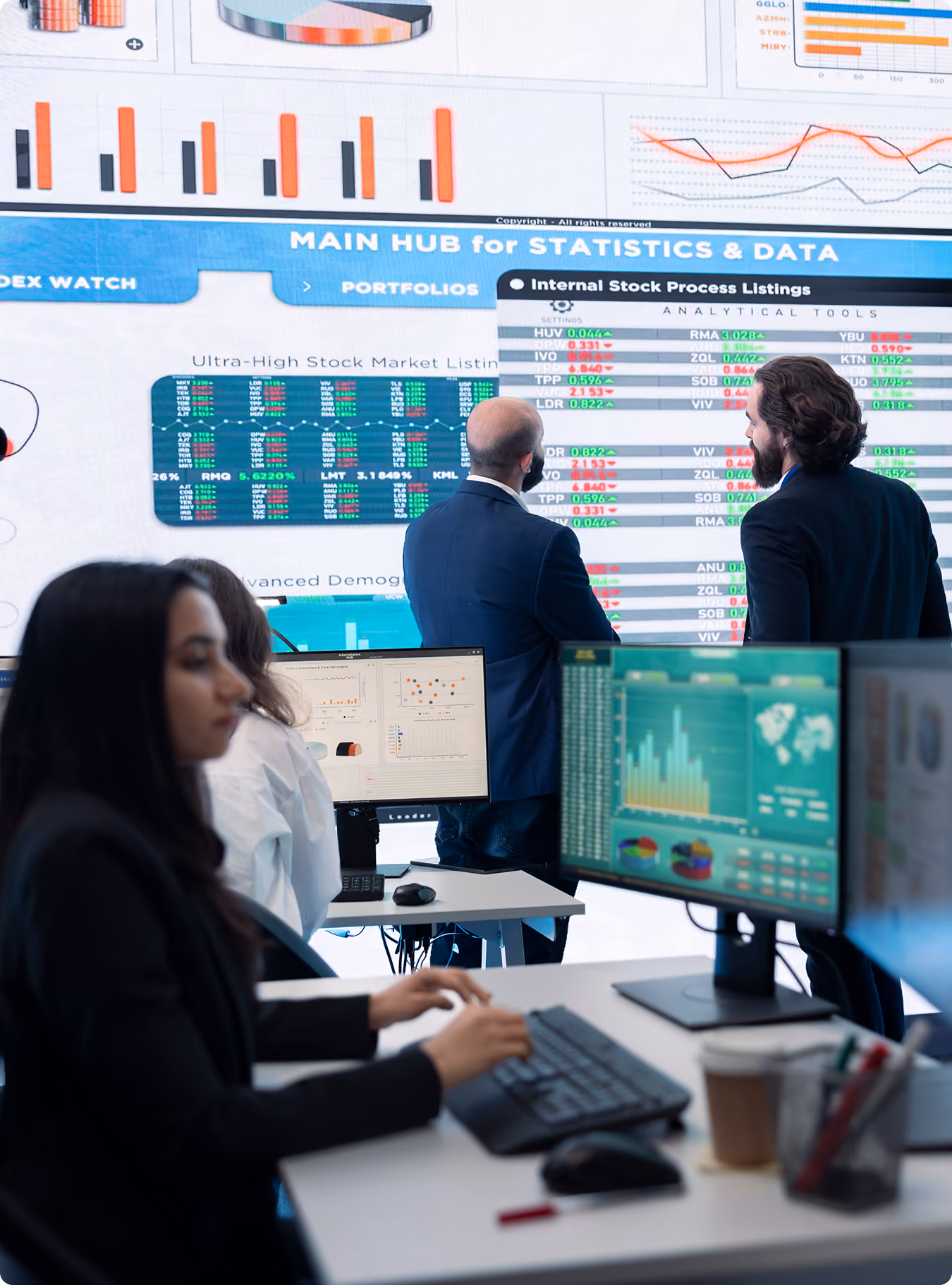 People working in a data center with multiple screens showing graphs and stock market statistics.