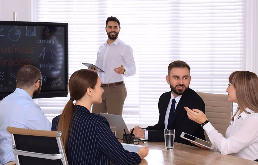 Businessman presenting with tablet while colleagues listen and discuss around a conference table.
