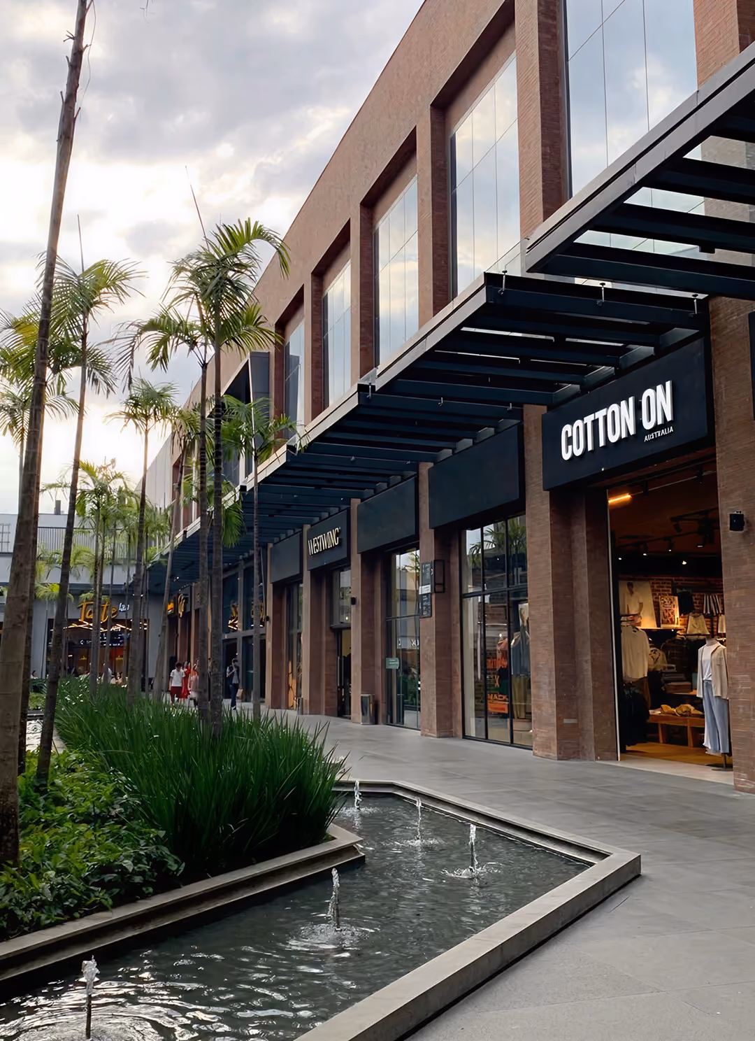 Modern shopping arcade with water fountains, palm trees, and stores including Cotton On Australia.