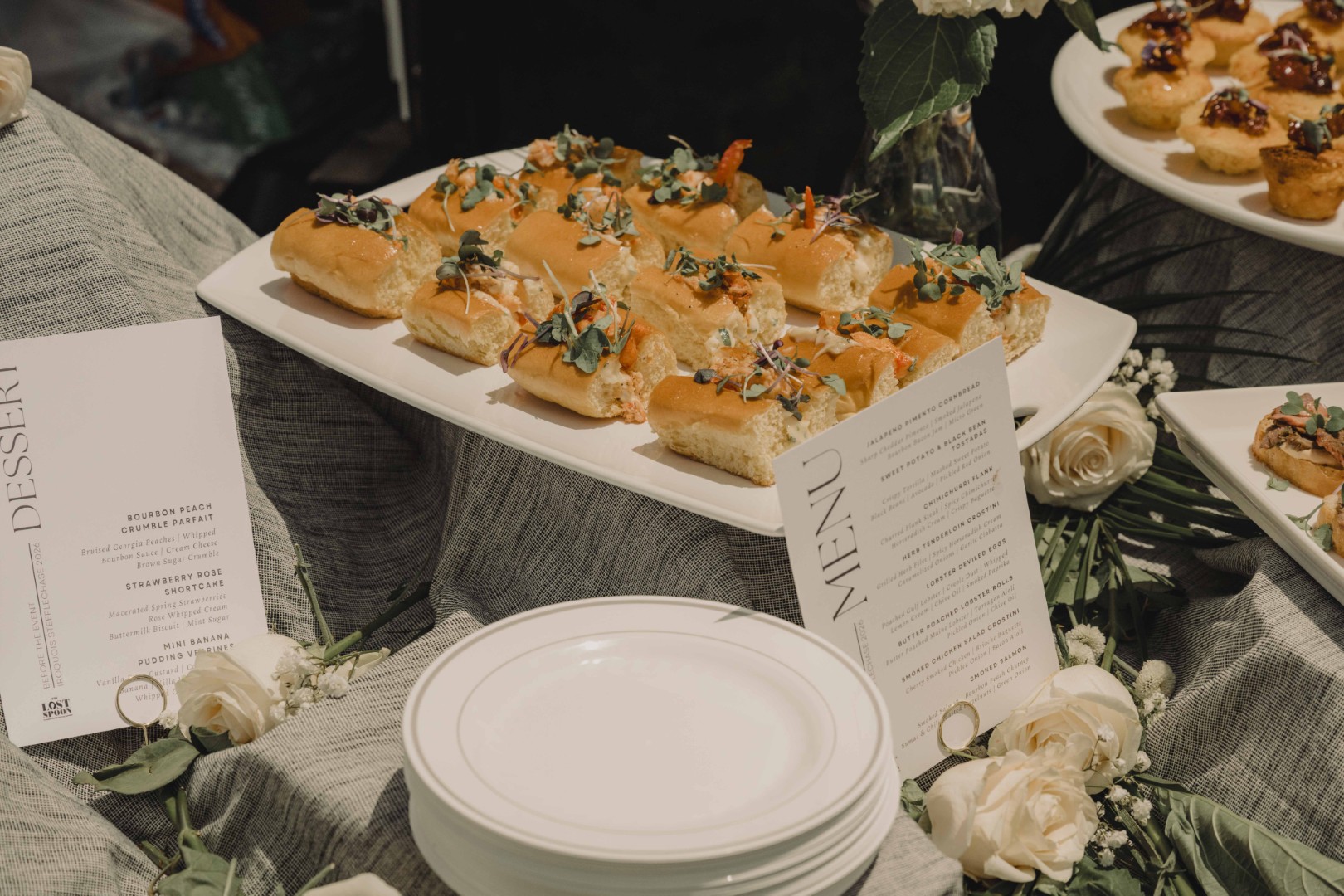 Outdoor art setup with small tables, canvases, and orange cushions on grass under leafy trees.
