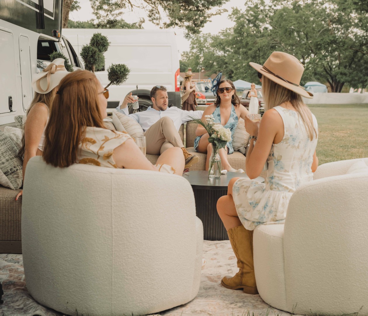 People gathered around a table with an assortment of sandwiches, appetizers, and drinks outdoors.