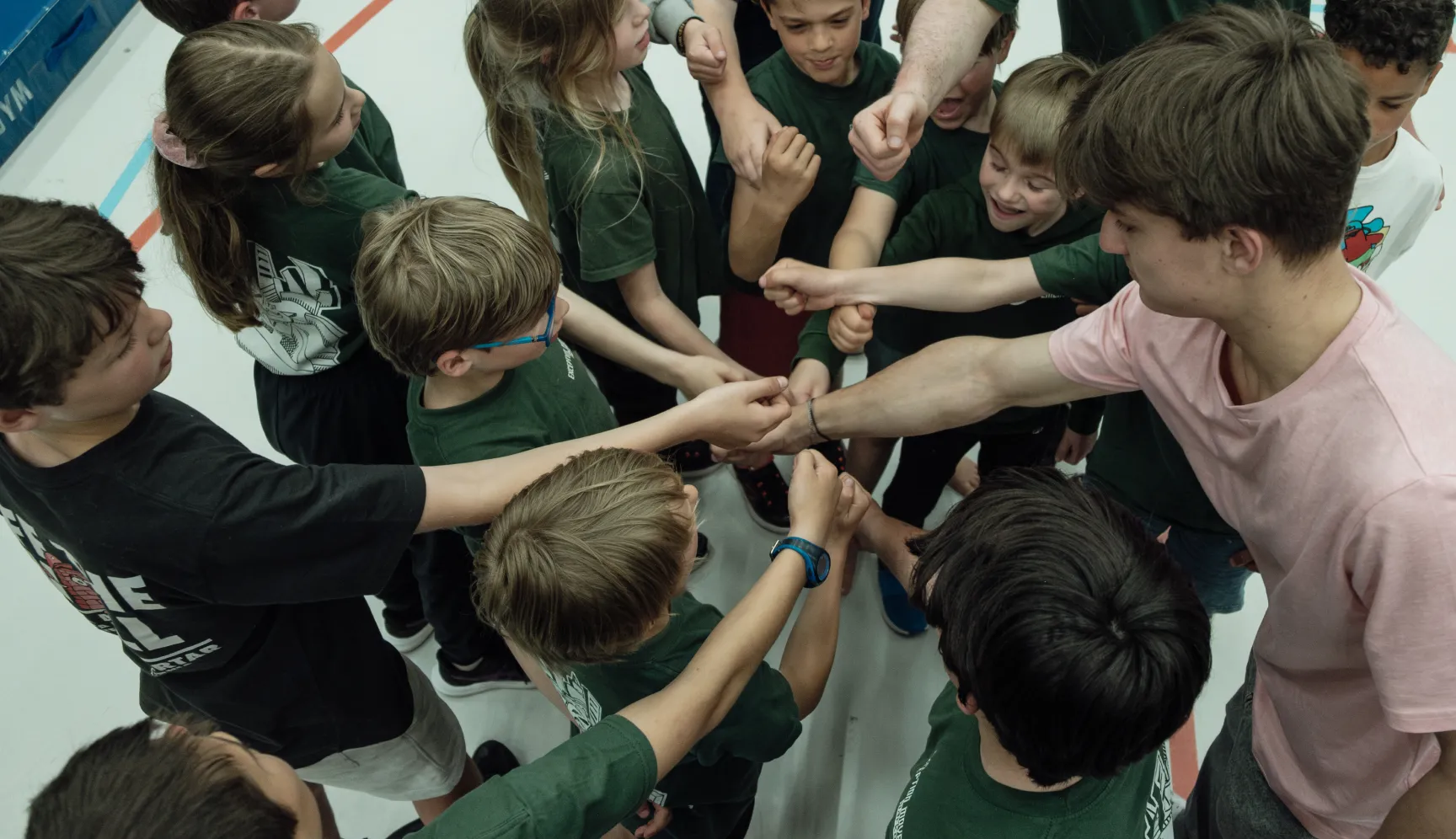 Kinderen en coaches steken hun handen samen in een teamcirkel