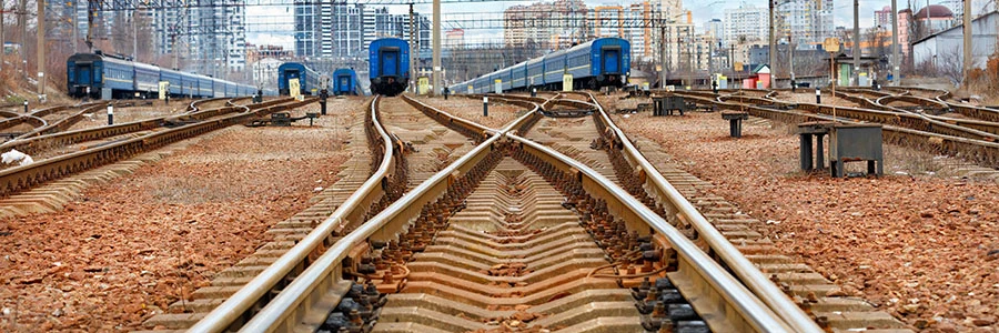 Railroad track switches and crossovers in railway classification yard with freight cars visible in background