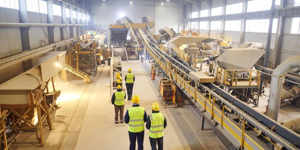 Workers in safety gear inspecting a mineral processing facility with conveyor systems and processing equipment.
