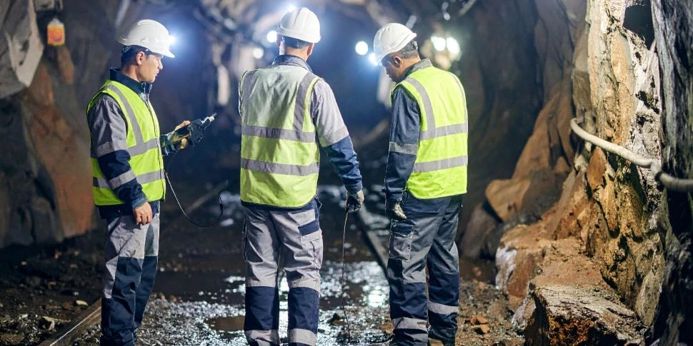 Mining engineers in safety gear inspecting underground tunnel with headlamps for safety compliance