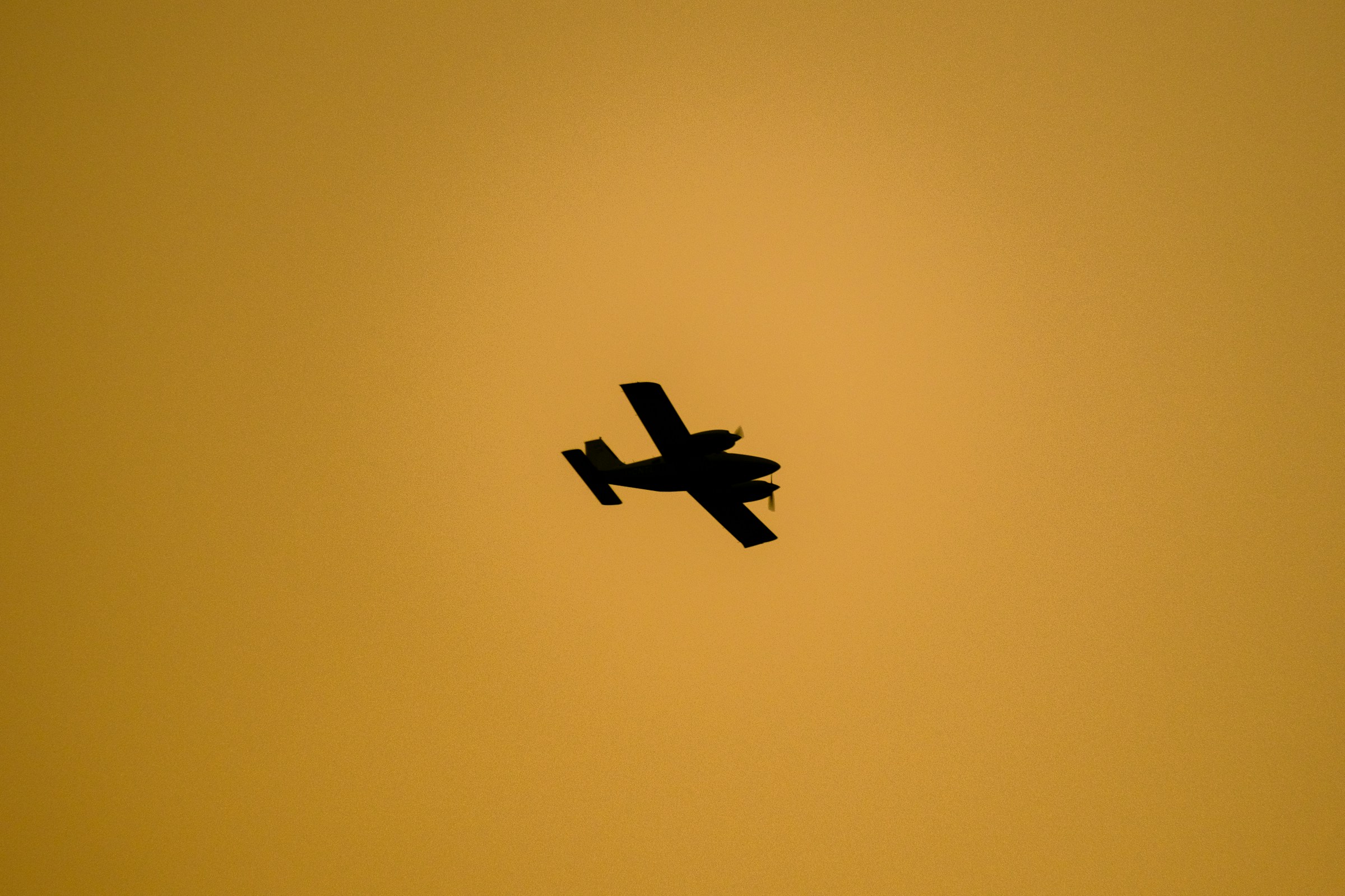 Small aircraft silhouette against vivid orange and yellow sunset sky