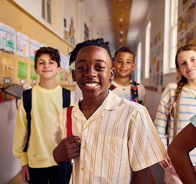 Respire Education | Group of smiling children with backpacks standing in a school hallway.